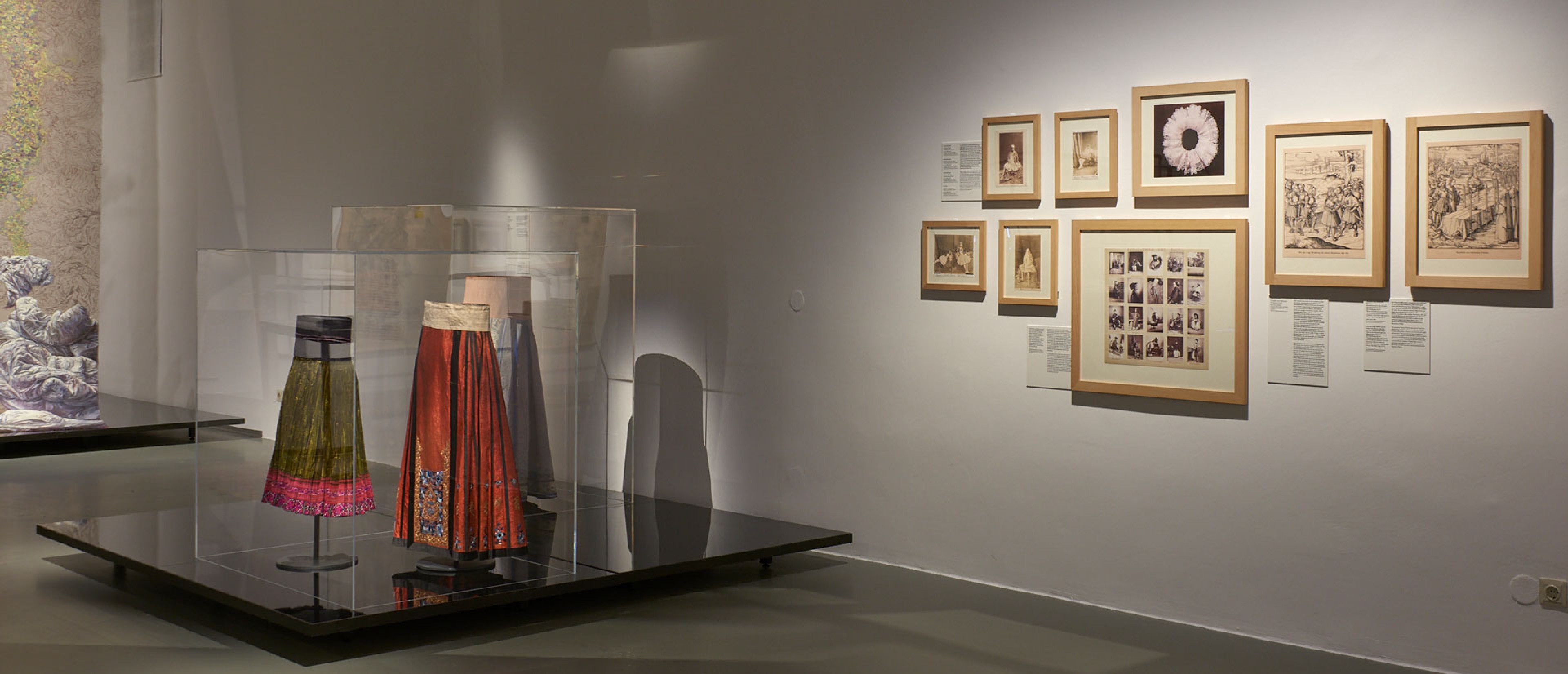 Exhibition space with objects: Pleated skirts, painting, photographs on the walls.