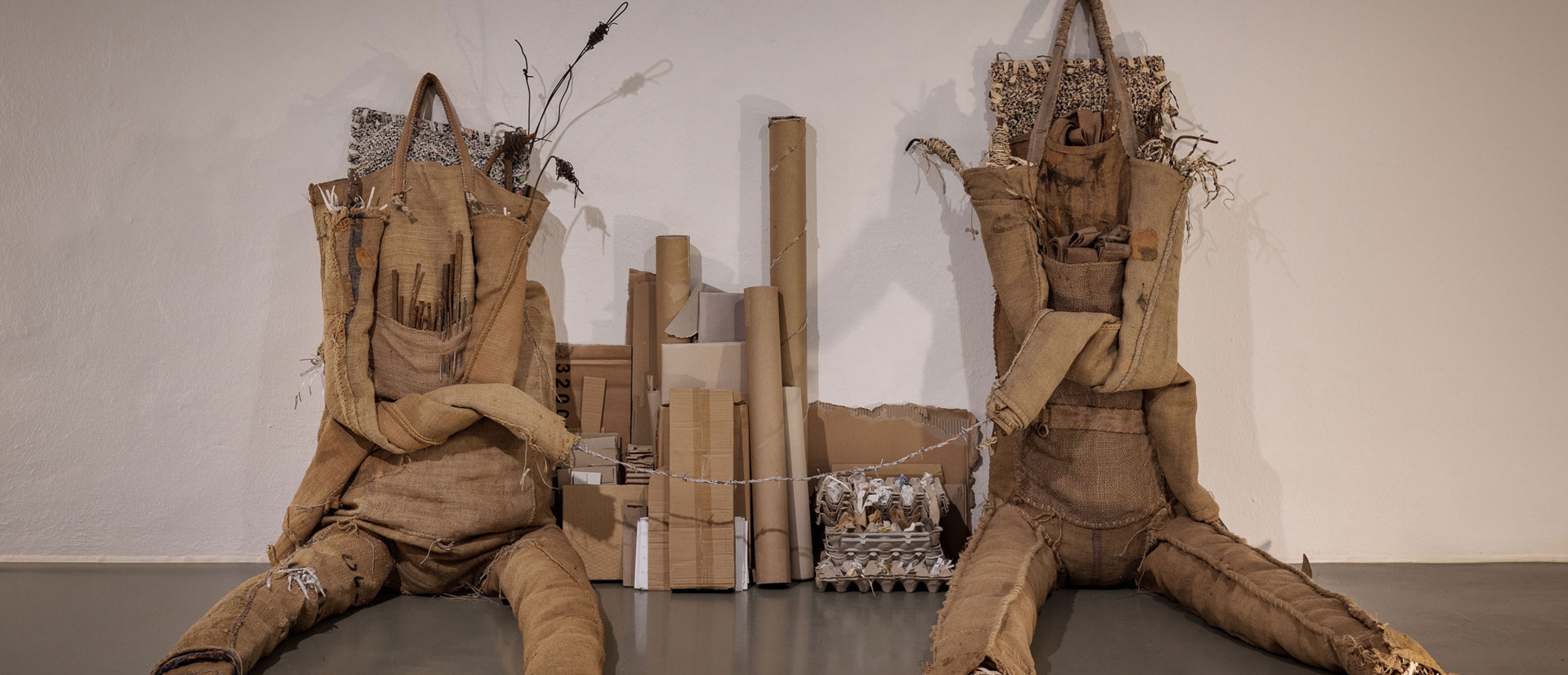 Two scupltures made of jute bags leaning against a wall. 